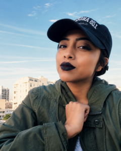 Aura Xec, Education is Forever scholarship recipient, poses outdoors in a green jacket and black cap, reflecting confidence and determination as she pursues her educational and career goals.